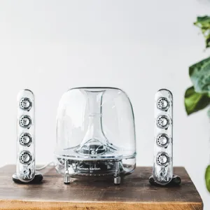 Harman Kardon transparent speaker set with a dome-shaped subwoofer and two vertical satellite speakers on a wooden surface.