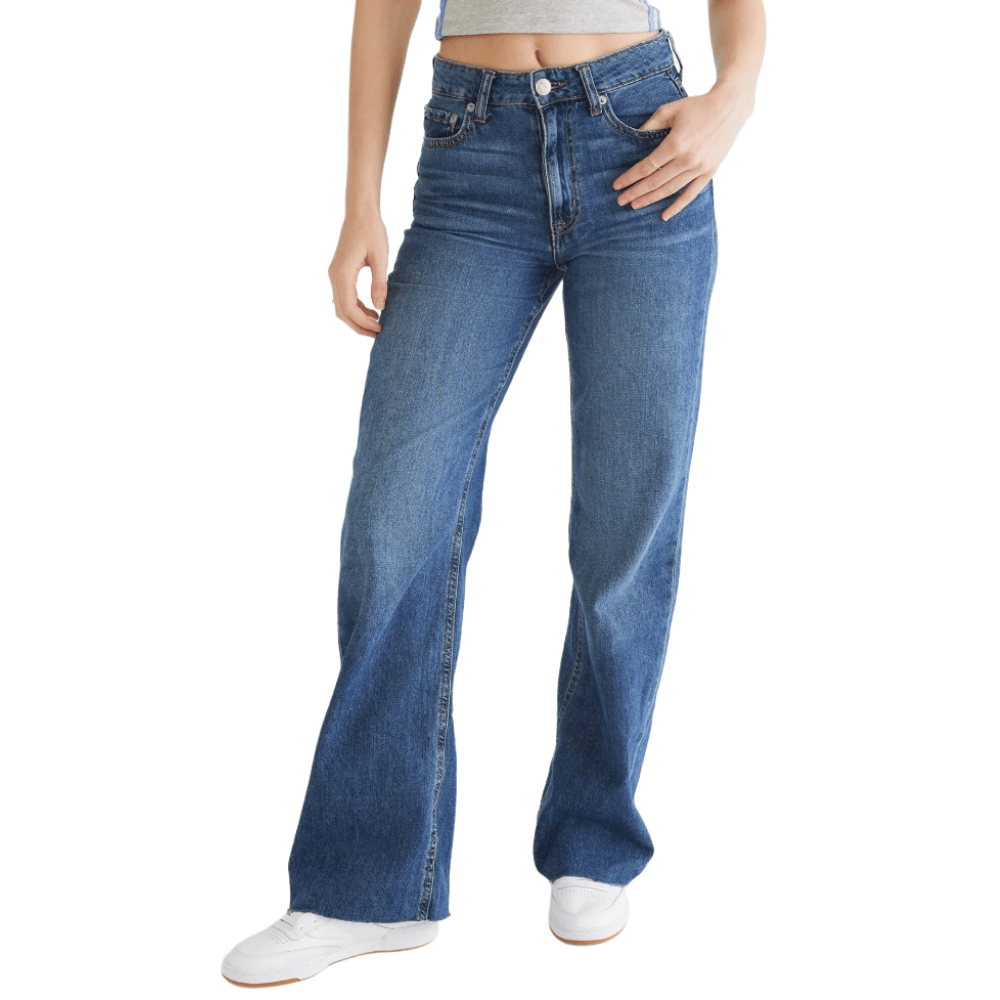 A person is wearing high-waisted blue flared jeans and white sneakers.