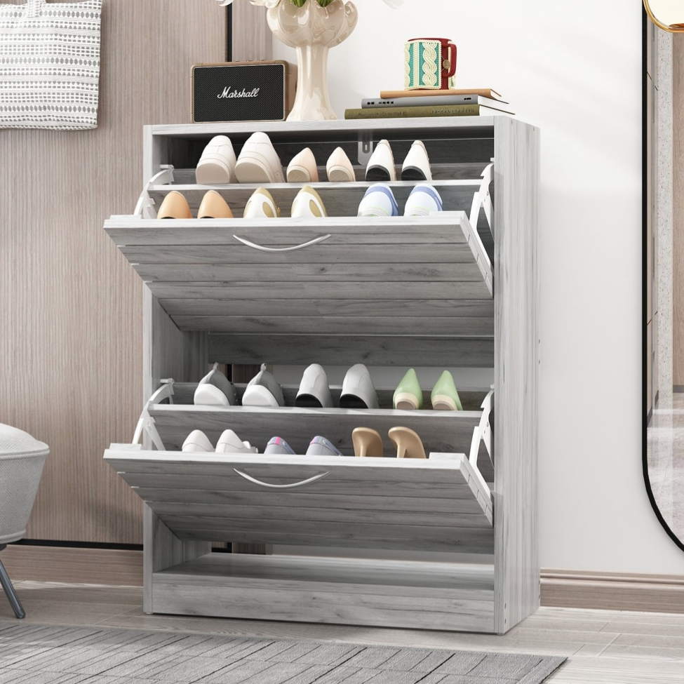 A multi-tiered shoe cabinet with pull-out drawers holds various pairs of shoes. Decorative items, including a vase with flowers and a mug, are placed on top.