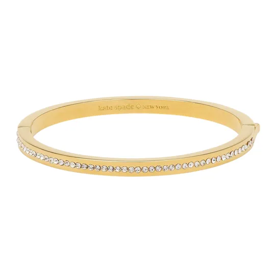 A gold-tone bangle bracelet featuring a row of small clear stones along the outer edge with an engraved \“kate spade NEW YORK\“ logo on the inner surface.