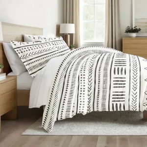 A bed is adorned with a duvet and pillowcases featuring a black and white geometric pattern. The room includes a wooden headboard, side tables, and a window with natural lighting.