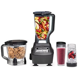 A Ninja Mega Kitchen System featuring a blender with a large pitcher filled with fruit, a food processor bowl with dough, and two single-serve cups for smoothies.