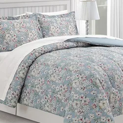 A floral-patterned bedding set featuring a blue background with white and pink flowers, accompanied by matching pillow shams and a white border.