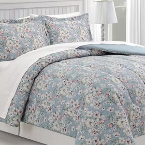 A floral-patterned bedding set featuring a blue background with white and pink flowers, accompanied by matching pillow shams and a white border.