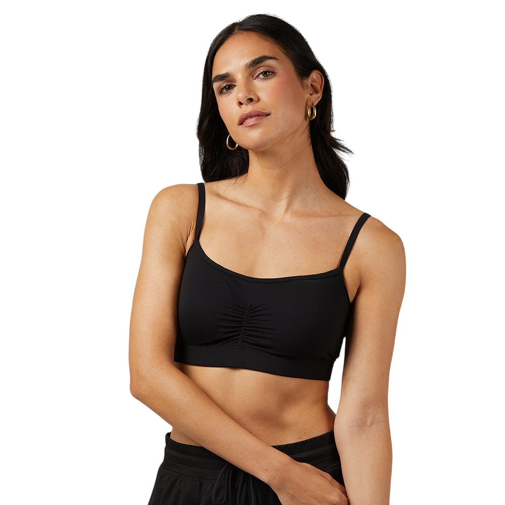 A woman is wearing a black camisole with adjustable thin straps and ruching detail at the front, paired with black pants.