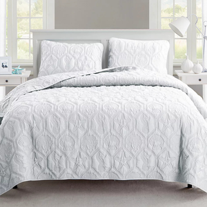 A white quilt with embossed sea-themed patterns including starfish, seashells, and seahorses is displayed on a bed with matching pillow shams.