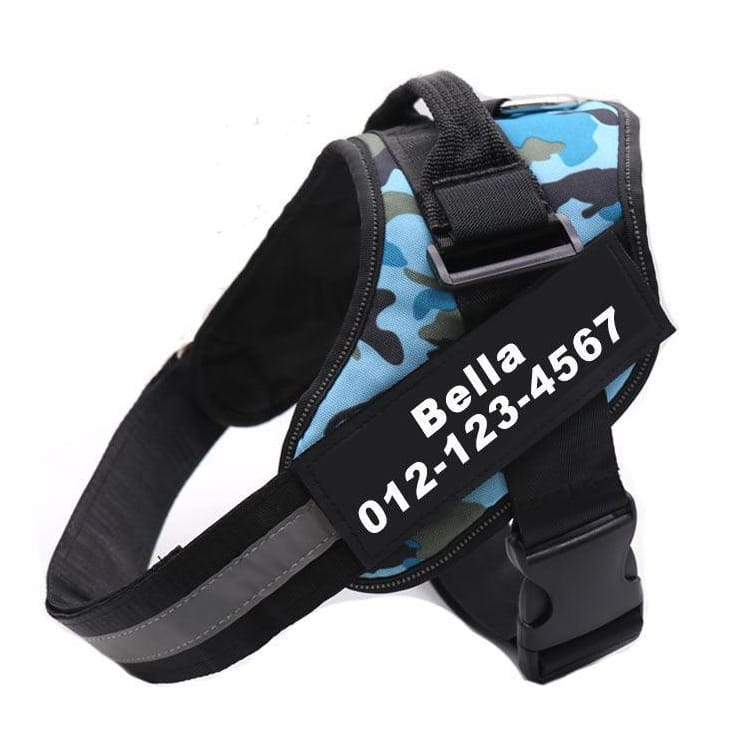 A blue camouflage dog harness with a handle, buckle, and reflective strap features a personalized patch displaying \“Bella\“ and the phone number \“012-123-4567.\“