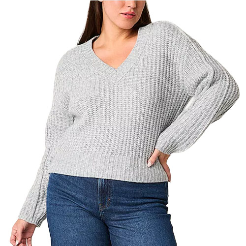 A person wearing a light gray, chunky knit V-neck sweater paired with blue jeans.
