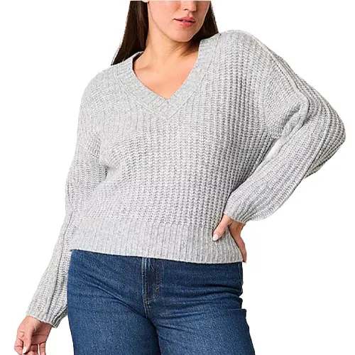 A person wearing a light gray, chunky knit V-neck sweater paired with blue jeans.