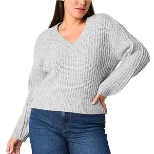 A person wearing a light gray, chunky knit V-neck sweater paired with blue jeans.