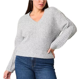 A person wearing a light gray, chunky knit V-neck sweater paired with blue jeans.