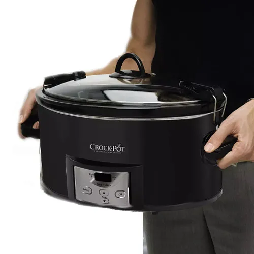 A person is holding a black Crock-Pot slow cooker with a digital control panel and a glass lid secured with metal latches.