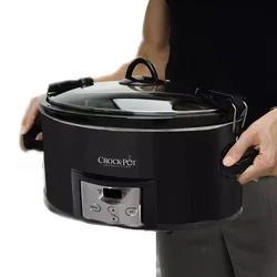 A person is holding a black Crock-Pot slow cooker with a digital control panel and a glass lid secured with metal latches.