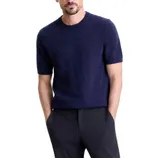 A man is wearing a short-sleeved navy knit sweater paired with dark pants.