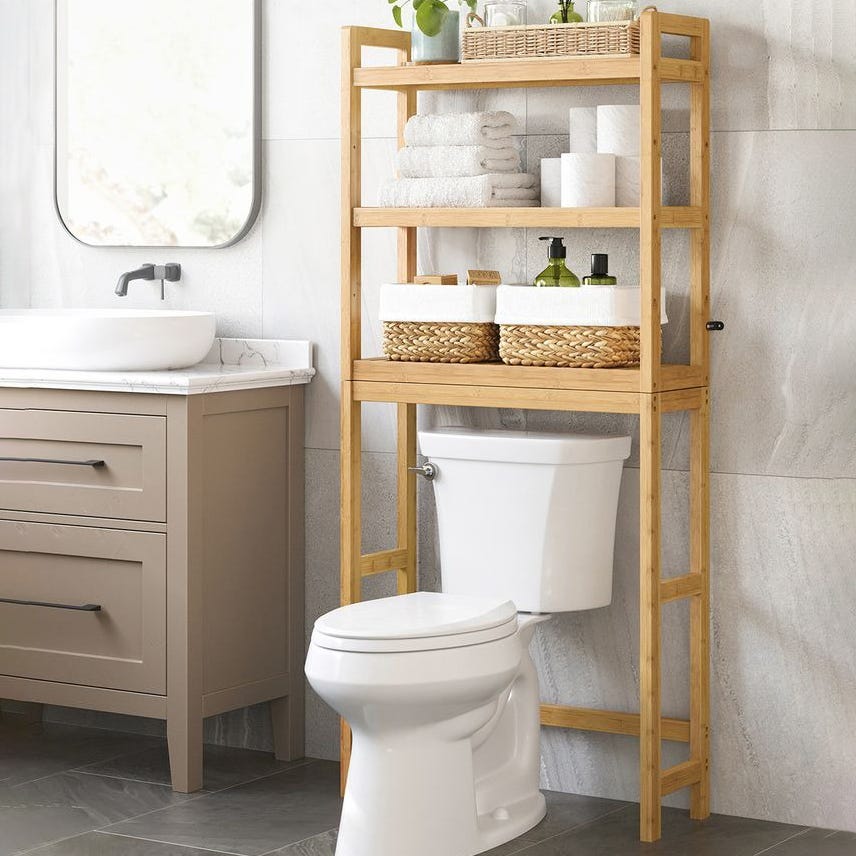 Bathroom features a wooden over-the-toilet shelf with towels, toilet paper, baskets, soap dispensers, and a potted plant, next to a vanity with a sink and mirror.