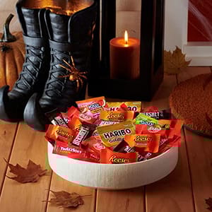 A variety of Hershey's Halloween candy, including Reese's, Twizzlers, and Haribo Goldbears, is displayed on a flat surface, accented by autumn leaves and a candle.