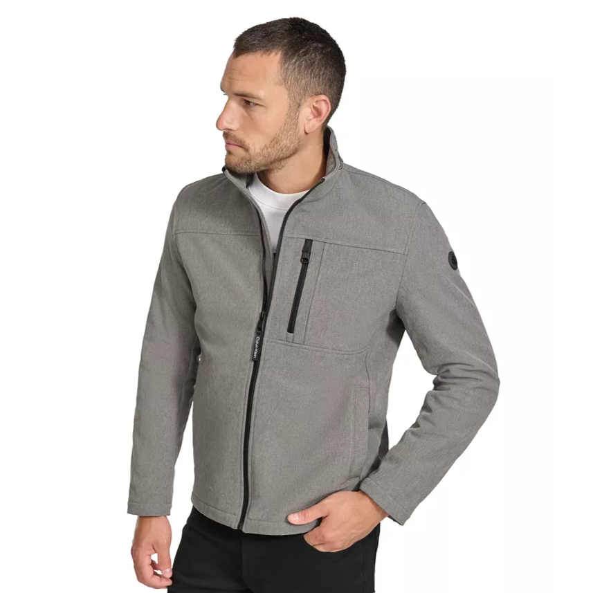 A man is wearing a gray zip-up jacket with black accents and a high collar. The jacket features two side pockets and a zippered chest pocket.