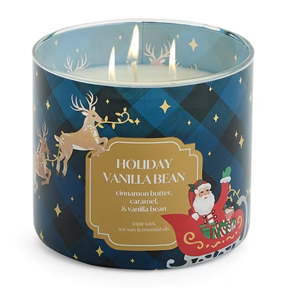 A three-wick candle labeled \“Holiday Vanilla Bean,\“ featuring scents of cinnamon butter, caramel, and vanilla bean. The design includes Santa in a sleigh and reindeer, set against a blue and black checkered pattern.