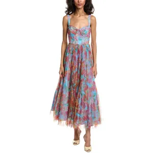 A woman is wearing a colorful floral-print midi dress with a fitted bodice, pleated skirt, and wide shoulder straps, paired with open-toe heels.