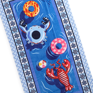 A beach towel features playful illustrations of a crab, lobster, colorful swim rings, and a beach ball, with a decorative border featuring geometric and floral patterns.