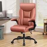 An ergonomic office chair with cushioned seat, high backrest, and adjustable armrests in a pinkish hue, placed in a home office setting with a wooden floor and desk.