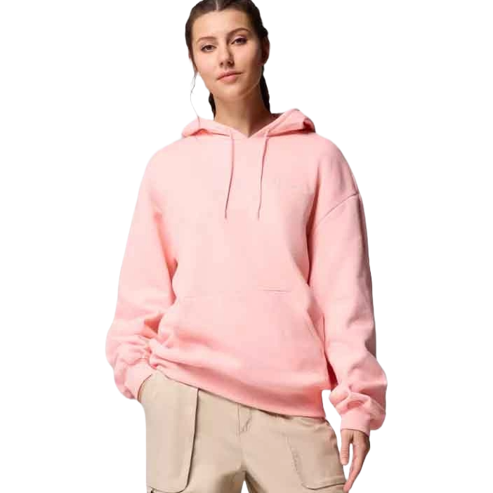 A young woman is wearing a light pink hoodie with a kangaroo pocket, paired with beige pants. The hoodie has a relaxed fit and drawstring hood.