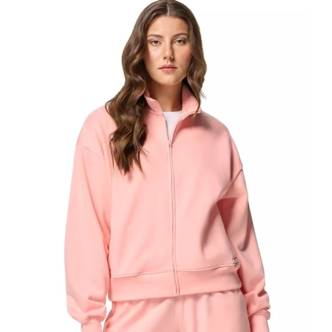 A woman is wearing a matching light pink zip-up sweatshirt and shorts set. The outfit has a casual and relaxed style.