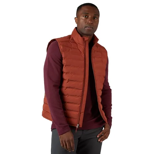 A man is wearing a rust-colored puffer vest over a maroon long-sleeve shirt and gray pants.