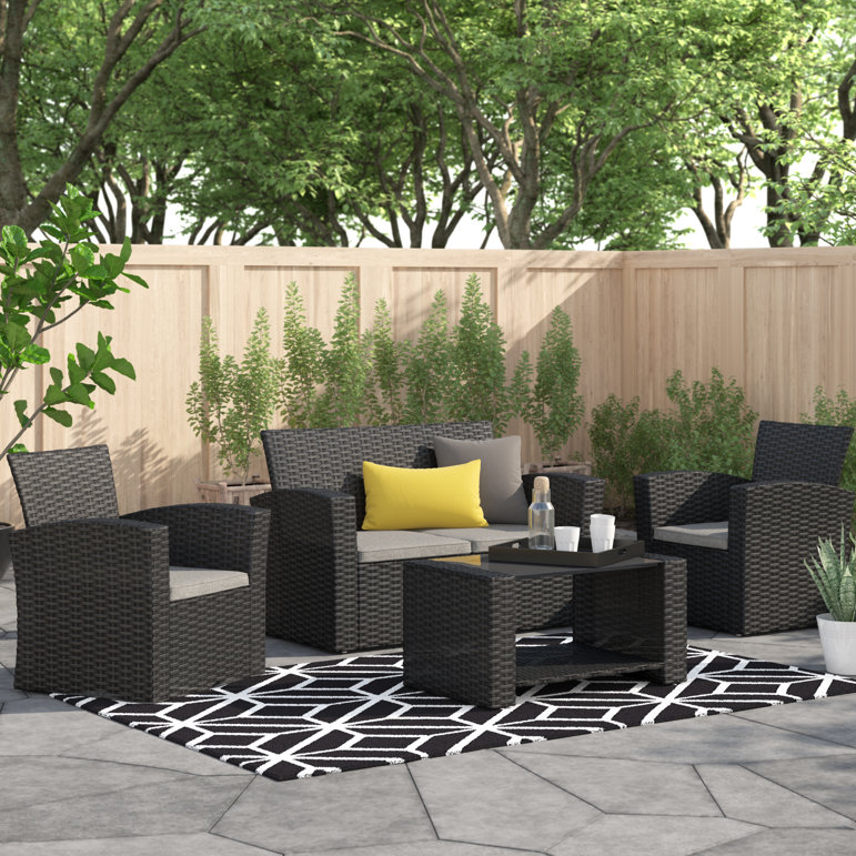 A 4-piece patio set featuring a sleek black rattan finish, including two armchairs, a loveseat with gray cushions, and a coffee table, all arranged on a geometric-patterned rug, with yellow and gray accent pillows enhancing the modern outdoor setting.
