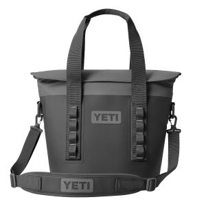A dark gray Yeti Soft Hopper cooler with sturdy handles and a detachable shoulder strap. It features a zipper closure, side loops for attachments, and the Yeti logo prominently displayed.