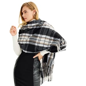 A woman is wearing a black and white plaid Nine West Soft-Touch Wrap Scarf with fringe detailing, styled draped over her shoulders. She pairs it with a black dress and white long-sleeve top.