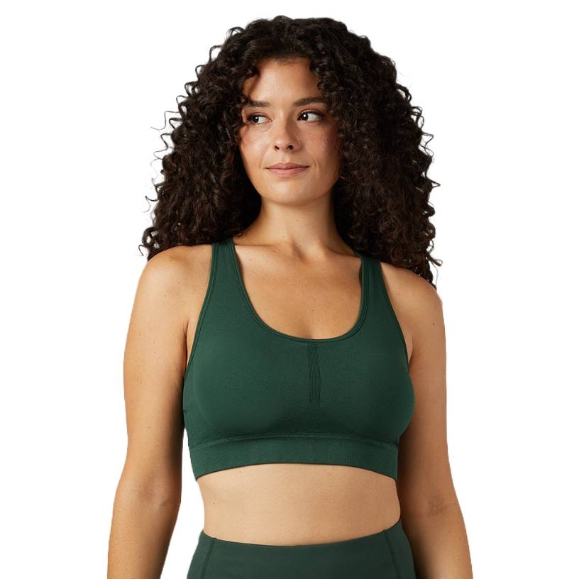 A woman wearing a dark green sports bra with a scoop neckline and racerback design, paired with matching leggings, standing in a relaxed posture.