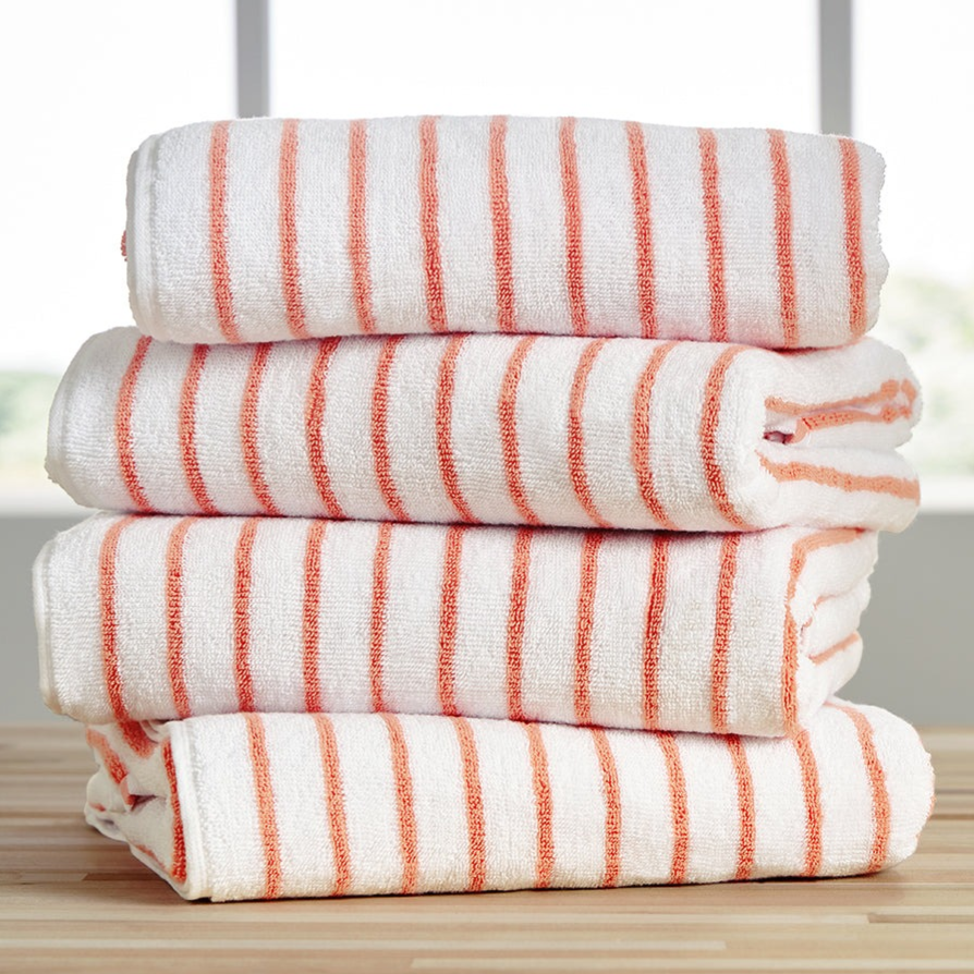Stack of four white towels with orange stripes on a wooden surface, against a blurred window background.