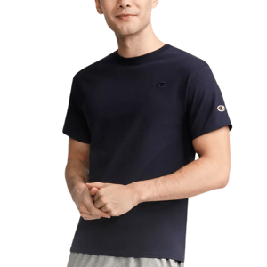 A person wears a navy blue Champion t-shirt with the brand's logo on the chest and sleeve, paired with gray pants.