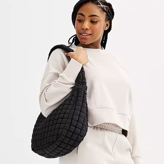 A woman wearing a white sweatshirt and carrying a black quilted shoulder bag.