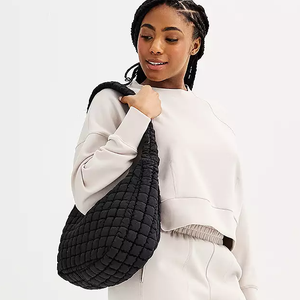 A woman wearing a white sweatshirt and carrying a black quilted shoulder bag.