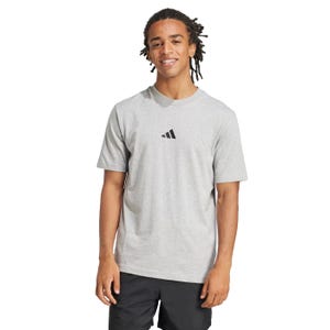 A person is wearing a light gray Adidas T-shirt with a small black logo in the center, paired with black shorts.