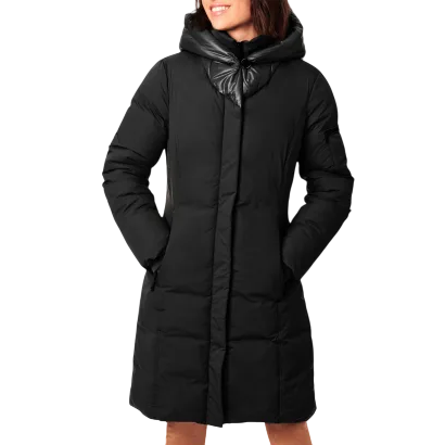 A woman wearing a black, knee-length puffer coat with a hood and front zip closure, styled over brown pants.