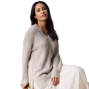A woman is modeling a beige Lauren Conrad tunic sweater with a V-neck and relaxed fit, paired with a light flowing skirt. The sweater features ribbed detailing on the cuffs and hem for subtle texture.