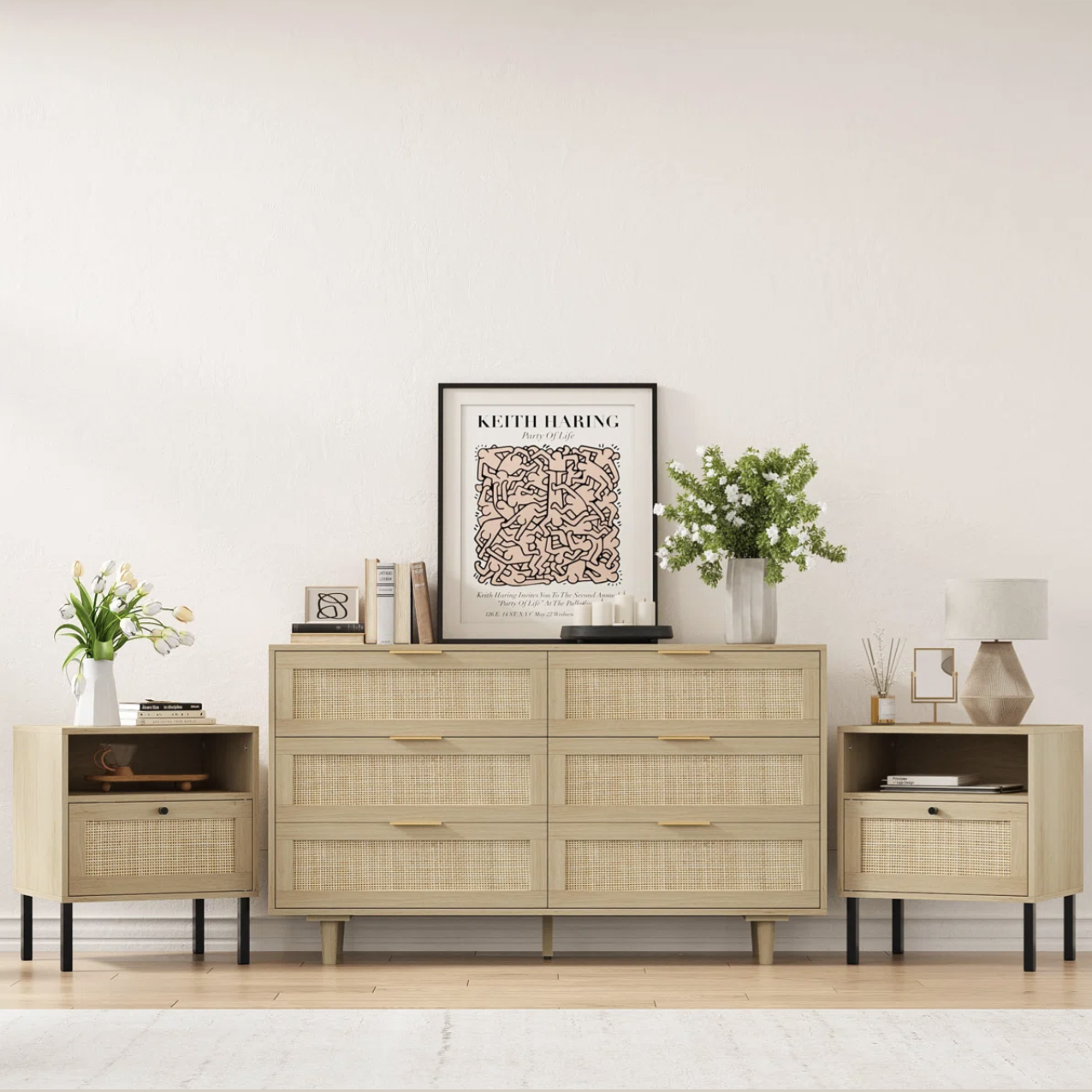 A stylish setup featuring a beige dresser with six drawers, flanked by two single-drawer nightstands, all with woven rattan fronts and black metal legs. Decor includes books, a framed print, flowers, and a lamp.
