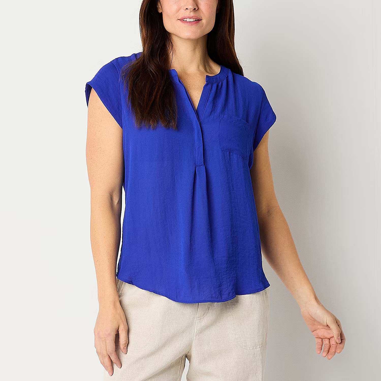 Woman wearing a blue short-sleeved blouse with a mandarin collar and a front pleat detail. She's also wearing beige trousers.