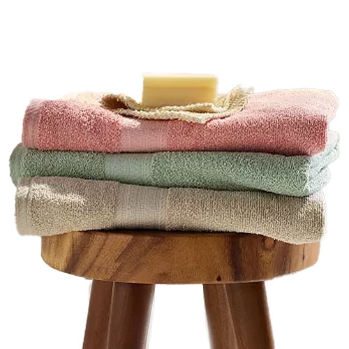 Three folded towels in pastel colors—pink, green, and beige—are stacked on a wooden stool with a bar of soap on top.