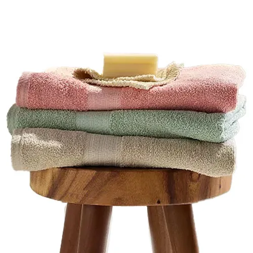 Three folded towels in pastel colors—pink, green, and beige—are stacked on a wooden stool with a bar of soap on top.