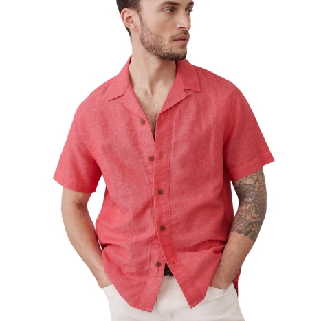 A man is wearing a short-sleeve, button-up red shirt with a collar and beige pants. He has a tattoo on his left forearm.