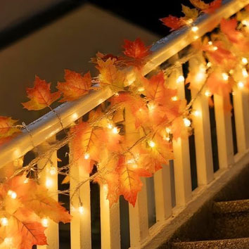 String lights with autumn leaves decor are wrapped around a stair railing.