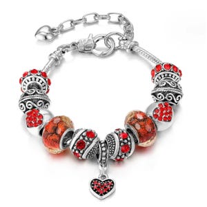 Silver charm bracelet with red crystal embellishments and a heart pendant.
