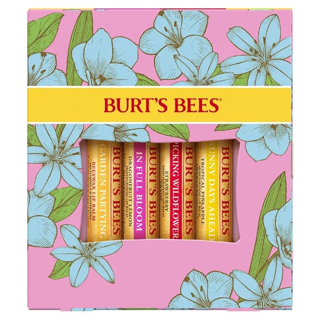 Burt's Bees In Full Bloom Lip Balm Set features four flavored lip balms: Garden Partying (Cucumber Mint), In Full Bloom (Dragonfruit Lemon), Picking Wildflowers (Sweet Mandarin), and Sunny Days Ahead (Tropical Pineapple), packaged in a floral-themed box.