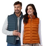 Two people wearing sleeveless quilted vests: one in blue and the other in orange. Both have front zippers and are layered over long-sleeve shirts.