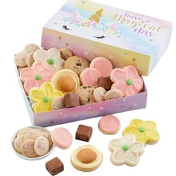 A pastel-colored box with \“Have a Magical Day\“ contains a variety of cookies, including flower-shaped, round pink, chocolate chip, and sprinkle-topped cookies, along with small fudge squares.