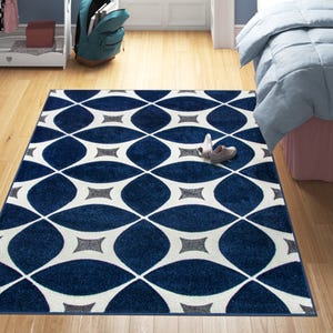 A rectangular area rug features a bold geometric pattern with interlocking curves in shades of navy blue and white, adding a modern touch to the room decor.